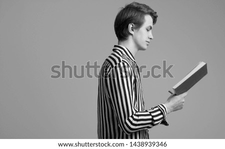 Fashion portrait of young handsome man in striped shirt reading a book on gray background in studio
