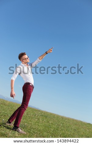full length picture of a casual young man standing outdoor and pointing and looking at the sun