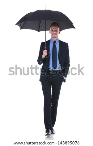 full length picture of a young business man walking towards the camera with an umbrella and his hand in his pocket while smiling. on white background