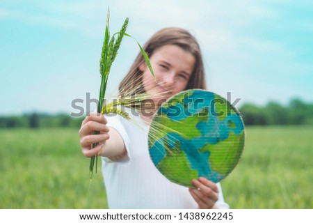 Teen girl holding planet and green spikelets of wheat in hands against green spring background. Earth day holiday concept. Protection and love of earth
