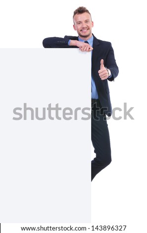 full length picture of a young business man holding a big empty pannel and the thumb up gesture while smiling at the camera. on white background
