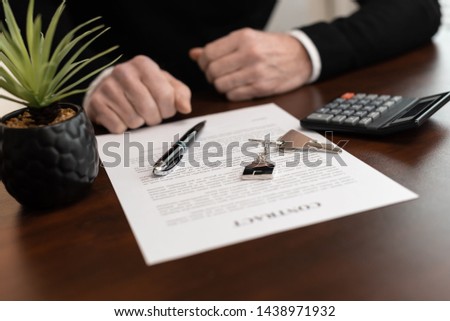 Hands of customer in front of real estate contract with house keys before signing