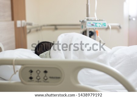 Close up back patient Asian young boy sleeping on bed and blurry set iv fluid intravenous drop saline drip in hospital room.Medical treatment concept.