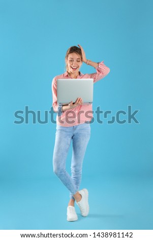 Full length portrait of surprised young woman in casual outfit with laptop on color background