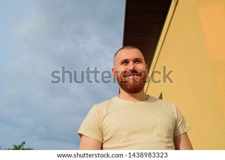 Male with trendy hairdo and beard, looks with serious expression, has thick red beard. Red-bearded man on the street in summer. Male 28-35 years old. The guy against the sky. The man is smiling. Royalty-Free Stock Photo #1438983323