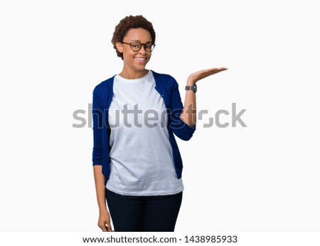 Young beautiful african american woman wearing glasses over isolated background smiling cheerful presenting and pointing with palm of hand looking at the camera.