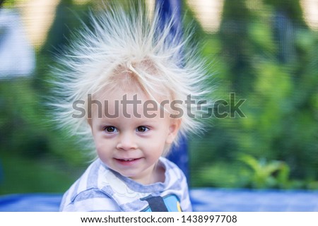 Cute little boy with static electricy hair, having his funny portrait taken outdoors on a trampoline Royalty-Free Stock Photo #1438997708