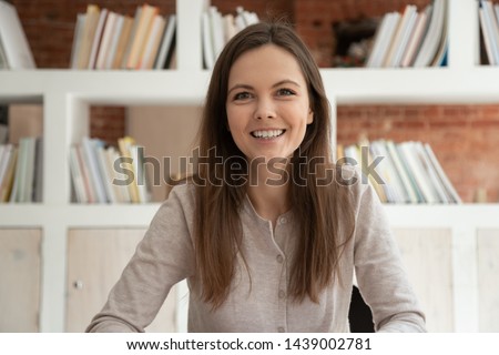 Smiling Caucasian girl look at camera having video call conversation or interview with employer, happy female millennial coach or tutor sit at desk shoot online training course or live tutorial Royalty-Free Stock Photo #1439002781