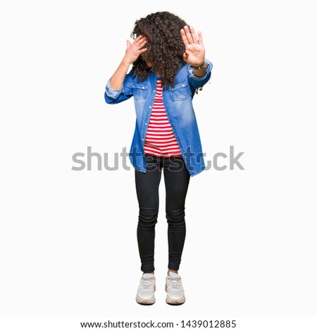 Young beautiful woman with curly hair wearing glasses covering eyes with hands and doing stop gesture with sad and fear expression. Embarrassed and negative concept.