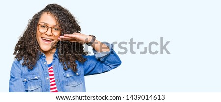 Young beautiful woman with curly hair wearing glasses gesturing with hands showing big and large size sign, measure symbol. Smiling looking at the camera. Measuring concept.