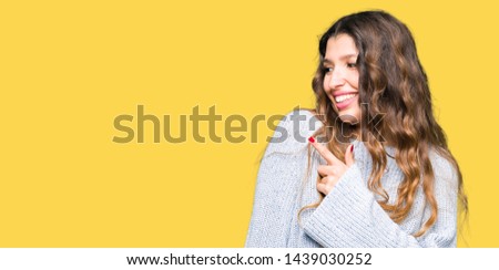 Young beautiful woman wearing winter sweater cheerful with a smile of face pointing with hand and finger up to the side with happy and natural expression on face