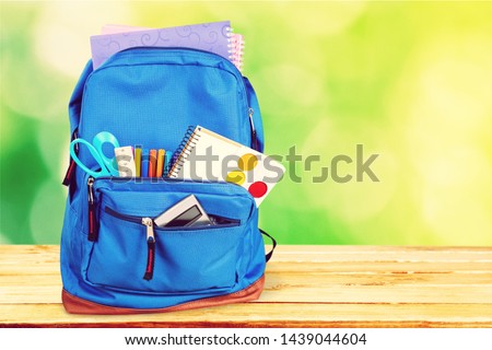 Open blue school backpack on wooden desk background.