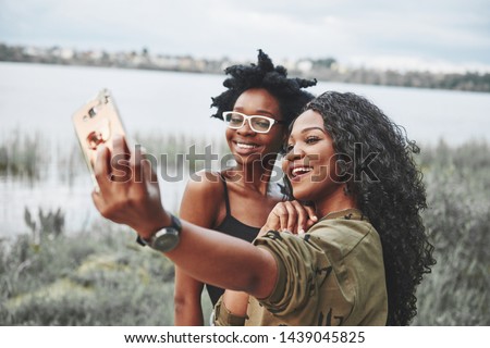 Two female afro american friends have a walk around beach. Taking selfie.