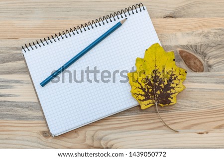 Blank school notebook with pencil and yellow autumn leaf on rustic wooden table. Back to school and education concept.