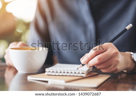 Closeup image of a woman writing on blank notebook while drinking coffee 