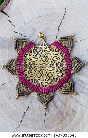 Brass metal pendant with macrame technique jewelry pendant on wooden background