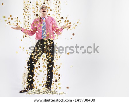 Full length of a happy male executive under shower of gold coins against white background