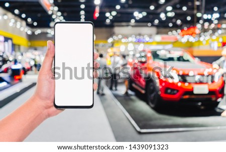 Mock up mobile phone. Hand holding mobile phone with abstract blurred cars exhibition show background image 