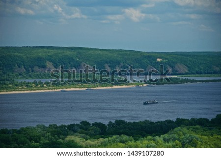 Wide river Volga near the city of Samara. Plain landscape. The steep bank of the river. Barge on the river. Forest to the horizon.