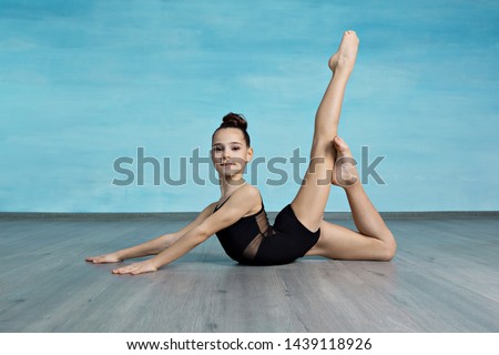 Girl gymnast smiles and shows a gymnastic exercise on the floor on a blue background
