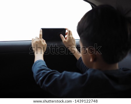 Asian boy siting inside a car and using smartphone to take a photo from outside. Selected focus. Isolated white background.