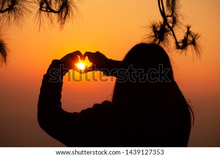 The silhouette picture, a girl hand up and make the love sign on the sunset sky