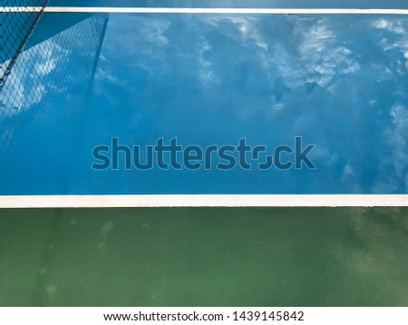 Tennis court after rain shower. Wet empty tennis court. Reflection of net and white cloud on the floor.