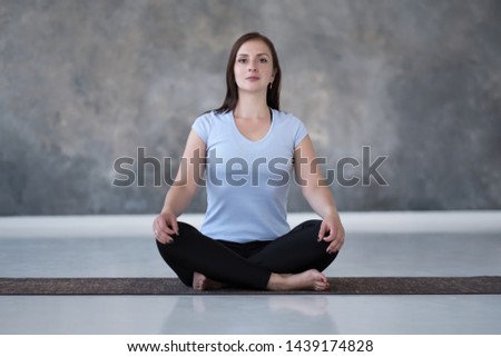 Young sporty woman practicing yoga, doing Sukhasana exercise, Easy Seat pose, working out. Indoor full length on gray background Royalty-Free Stock Photo #1439174828