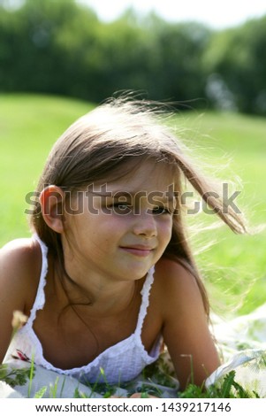 fanny and beautiful laughing little girl with long blond hair, outdoor portrait in summer park on bright sunny day. child in green grass field closeup portrait.