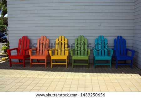 Rainbow colors of  Adirondack chairs in a row outside.  