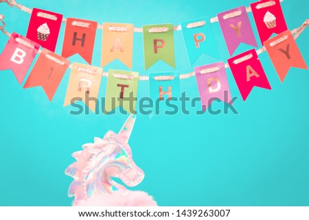 Shiny zine type holographic iridescent head of pink soft fluffy toy unicorn on bright blue background with Happy Birthday bunting above. Celebration or birthday greeting card concept with copy space