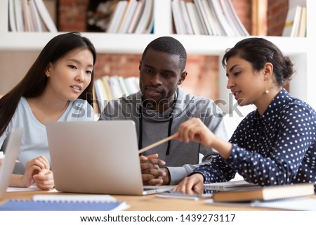 Multiethnic diverse students sit at desk look at laptop screen working together at school project, multiracial young people study at computer in group discuss share ideas collaborate in classroom Royalty-Free Stock Photo #1439273117