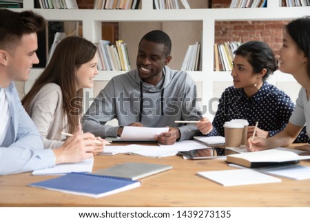 Happy multiracial people sit at shared table talk and laugh studying in library prepare for test together, smiling diverse mixed international group have fun engaged in teambuilding activity in class Royalty-Free Stock Photo #1439273135