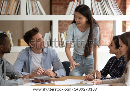 Motivated Asian female team leader stand hold meeting with mates talk discuss project or assignment, focused young ethnic girl speaker or tutor speak with students at group gathering. Teamwork concept Royalty-Free Stock Photo #1439273189