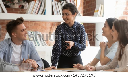 Concentrated indian girl stand talking with diverse young people discuss project working collaborating together, motivated female team leader hold students meeting share ideas with groupmates Royalty-Free Stock Photo #1439273195