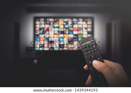 Multimedia video concept on TV set in dark room. Man watching TV with remote control in hand. Royalty-Free Stock Photo #1439344193