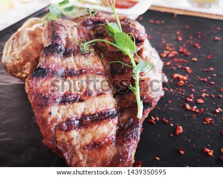 Fried pork on a black background. Grilled steak served on a black stone plate on a wooden table. With tomato sauce