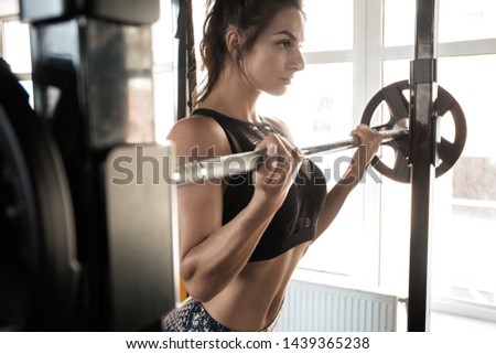 Attractive woman training in light modern gym. Beautiful muscular fit woman exercising building muscles