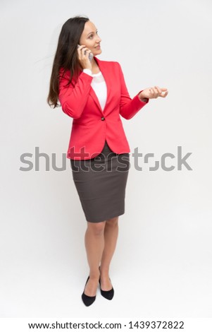 Full-length portrait of a young pretty brunette woman 30 years old in a bright red business suit with beautiful dark hair. Standing on a white background, talking, showing hands, with emotions