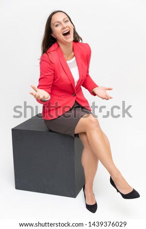 Full-length portrait of a young pretty brunette woman 30 years old in a bright red business suit with beautiful dark hair. Sits on a white background, talking, showing hands, with emotions