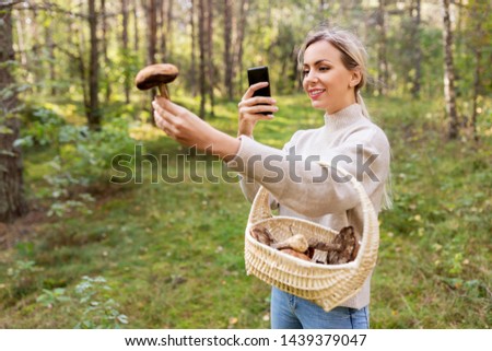 technology, people and leisure people concept - young woman with smartphone using app to identify mushroom in forest