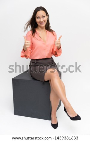 Full-length portrait of a young pretty brunette woman 30 years old in business clothes with beautiful dark hair. Sits on a white background, talking, showing hands, with emotions