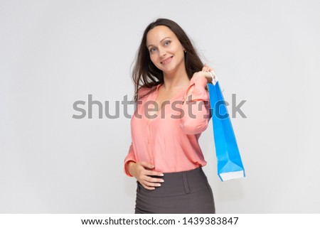 Portrait to the waist of a young pretty brunette woman of 30 years in business clothes with beautiful dark hair with a blue shopping bag. On a white background, talking, showing hands, with emotions