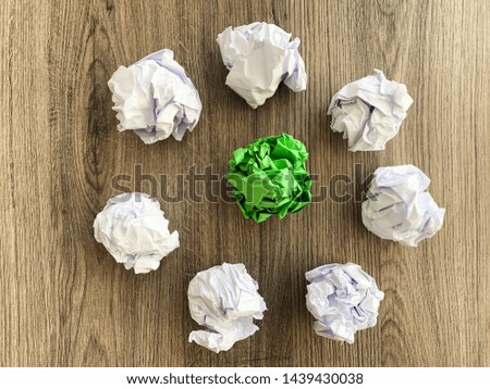 Crumpled green paper ball among white balls.