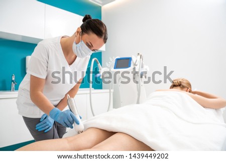 Waist up of doctor-massagist working with a massager on the buttocks and legs of young woman. Masseur makes her job with modern apparatus of figure correction. Body weight loss and anti cellulite