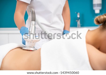 Cropped photo of Caucasian masseur wearing blue rubber gloves and making massage procedure on back of her client. Female patient lying on massage table and relaxing. Body weight loss and anti