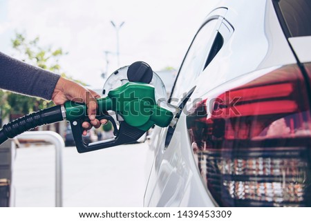 Man Handle pumping gasoline fuel nozzle to refuel. Vehicle fueling facility at petrol station. White car at gas station being filled with fuel. Transportation and ownership concept. Royalty-Free Stock Photo #1439453309