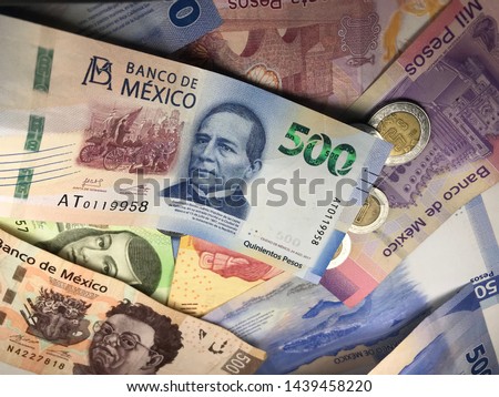 Many mexican pesos and other latin american money bills spread over a wooden desk inside a small business office