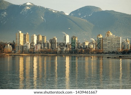 Vancouver's West End neighbourhood reflects in the waters of English Bay while Grouse Mountain rises in the background on a crisp Winter's morning.