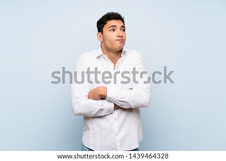 Handsome man over blue wall making doubts gesture while lifting the shoulders